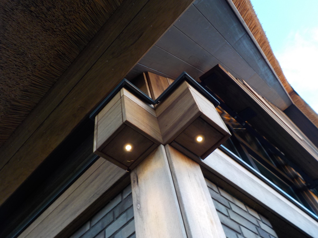 Post & beam kolommen en balken van Fraké Noir hout voorzien van LED-verlichting als  accentverlichting. Bijzondere detaillering samenkomt Post & Beam Fraké Noir hout, antraciet pointerwerk metselwerk en de kapconstructie met  onderliggende puien en Fraké Noir lamellen.